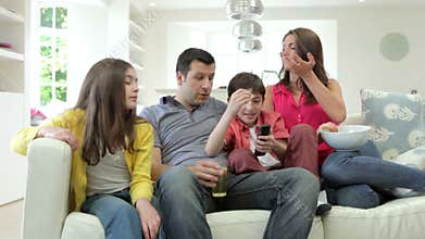 Hispanic Family Sitting On Sofa Watching TV Together