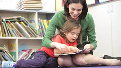 Teacher Reading Book With Female Pupil