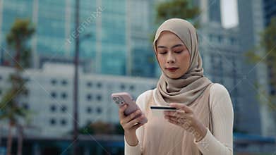 Portrait of Muslim woman pays online uses credit card and smartphone on street