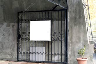 White blank sign hanging on an elegant black metal gate of a building with concrete walls, ideal for mockups