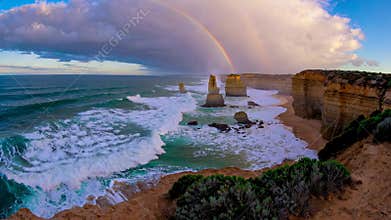 Scenic coastal view of the twelve apostles with vibrant rainbow over ocean waves and dramatic sky during sunset. Natural
