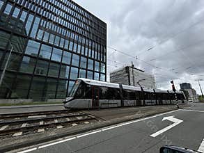 Modern tram crossing busy street beside glass office tower and wrapped