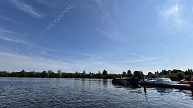 Wide calm waters beneath bright blue sky beside moored boats and tree