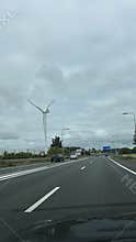 Multi lane highway leading past tall wind turbine under heavy cloudy sky