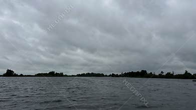 Wide lake under heavy gray clouds with low tree-lined horizon and