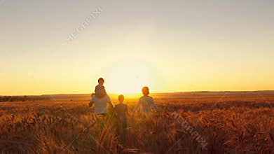 Happy family is walking along the wheat field at sunset.
