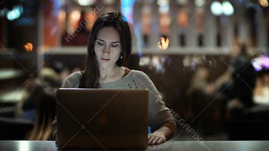 Young beautiful woman coming to cafe, sitting at the table and start to working on laptop. Female in city in the evening