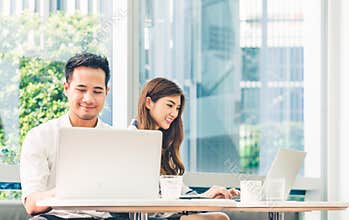 Young Asian couple or college student using laptop computer notebook work together at coffee shop or university campus
