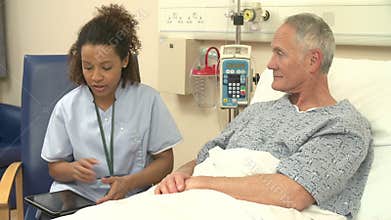 Nurse Sitting By Male Patient's Bed Using Digital Tablet