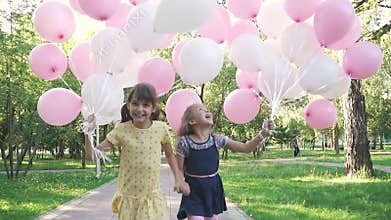 Two little girls gleefully run through the summer the Park with balloons in his hands. little sisters holding hands and