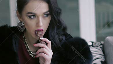 Glamorous brunette sitting, looking aside and touching chocolate by lips. Slowly