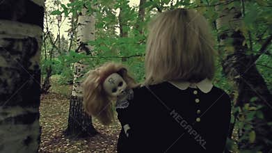 Stylized shot creepy white faced woman with a doll in the grass in the woods