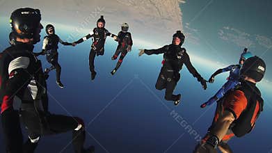 Group of skydivers jump from airplane, make formation in blue sky. Sun. Extreme