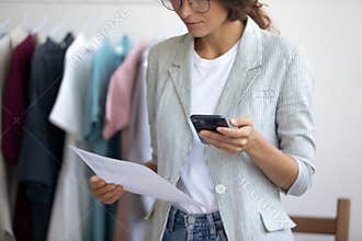 Focused female fashion designer consider paperwork using cell