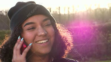 African American girl teenager young woman wearing a black beanie hat talking on mobile cell phone backlit by the sun