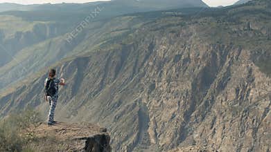 Girl tourist comes to the edge of the cliff having achieved success looking forward. Overall plan