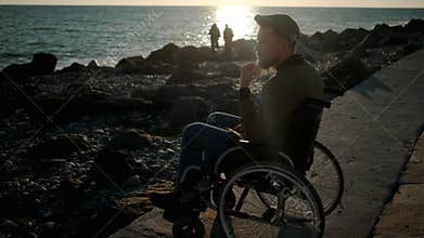 Male wheelchair user is looking on sea and thinking in spring evening