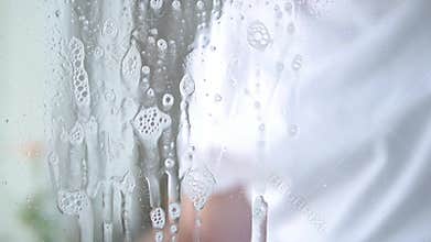 Close up man hands with blue gloves cleaning a window using sprayed liquid