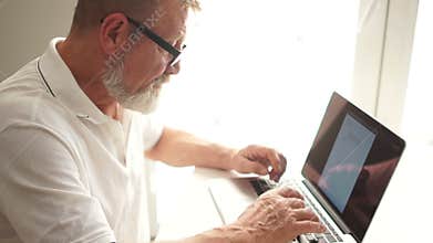 Mature man using a laptop to work at home. Writer or scientist at work. Senior citizen writes a letter using a computer