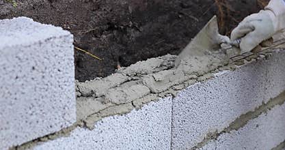 bricklayer building wall from ceramsite concrete blocks, applying mortar