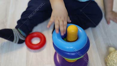 Little child one year old studies to collect colorful pyramid, close up