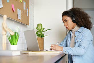 African teen girl student wearing headphones learning with online tutor at home.