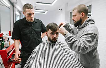 Barbershop. Professional barber teaches a student to cut a model in a men`s shop. Two men trimming a bearded model in a barbersho