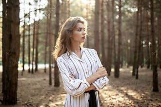 Beautiful young woman standing in the park with cross hands and looking at the side, in the sunny day