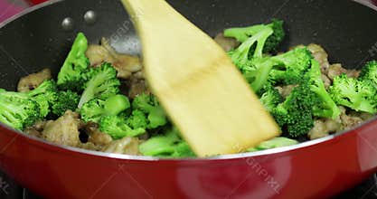 Woman cooking pork and broccoli in a red skillet