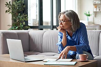 Senior older woman watching webinar on laptop working from home.