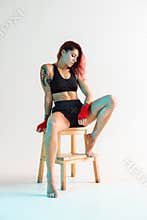 A young boxer girl with red bandages on her hands poses on a chair in a photo Studio.