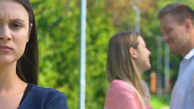 Displeased woman standing against happy couple of best friend and ex-boyfriend