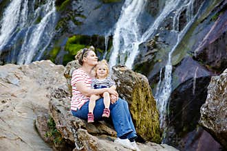 Cute toddler girl and mother sitting near water cascade of Powerscourt Waterfall, the highest waterfall in Ireland in co
