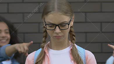 Mean teenagers pointing fingers at girl in eyeglasses, cruelty and hate of peers