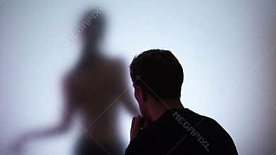 Man looking naked woman seductively dancing behind glass in night club, desire