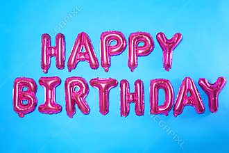 Phrase HAPPY BIRTHDAY made of pink foil balloon letters on blue background