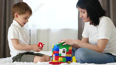 Happy family: mother and son playing with color blocks on white bed at home