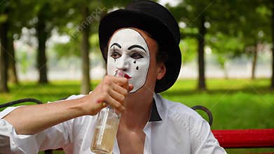 Close-up of a mime drinks alcohol outdoors. Bad habits