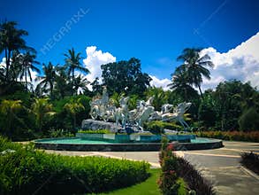 Blue Sky Krisna Eco Garden Park With Krishna`s Chariot Statue In The Middle Of The Pond Fountain On A Sunny Day