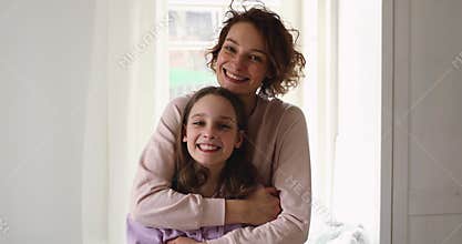 Happy affectionate young mom hugging teen daughter looking at camera