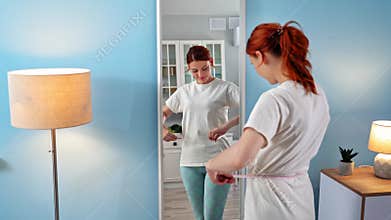 weight loss, a joyful young woman goes to the mirror and measures her waist with a sewing meter, rejoices at the result