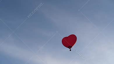 Colorful heart-shaped balloon flying at sunset over blue sky in slow motion, Happy Valentine's Day concept. high