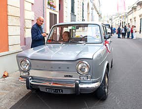 An old Italian married couple near their retro car