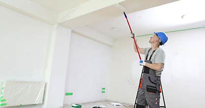 Man paints the ceiling with white paint using paint roller