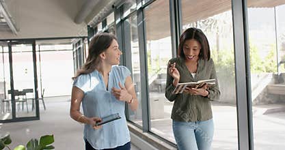 Two diverse businesswomen discussing with each other while walking in office