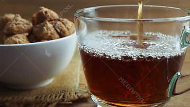 Pouring hot tea into transparent glass cup.