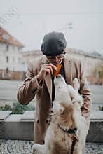 Happy senior man in elegant clothes training his big white dog in city during autumn day.