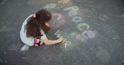 Little girl writing peace with chalk. Cute little girl drawing peace on the pavement with chalk. Protest against war, Russia