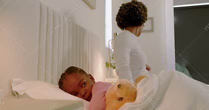 African American mother in bed, noticing daughter waking, using thermometer, giving medicine