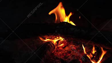 Flames flicker and crackle as they consume wooden logs, providing warmth and ambiance on a chilly night